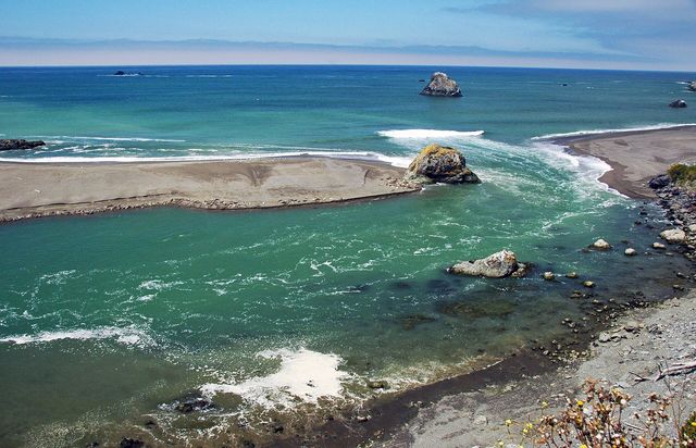 The Russian River meets the Pacific, swirling green past a sandbar and sea stack