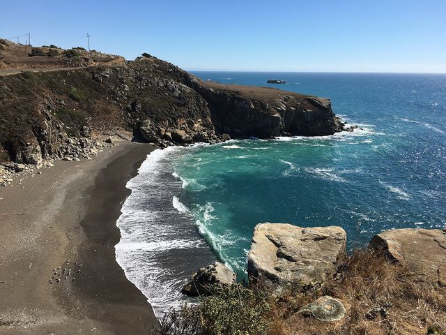 Turquoise surf and a dark-sand cove below the cliffs at Kolmer Gulch